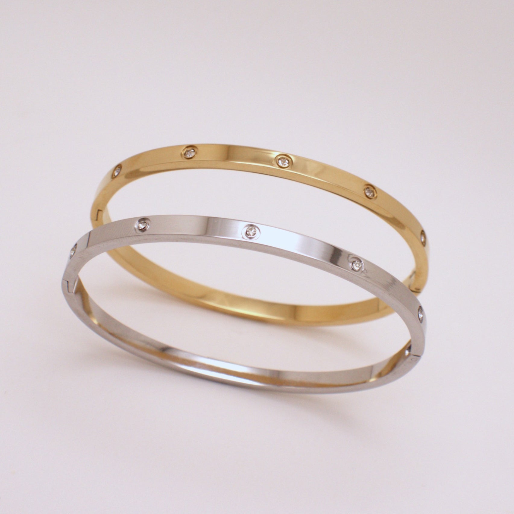 Two gold and silver bangles with embedded stones on a light pink background