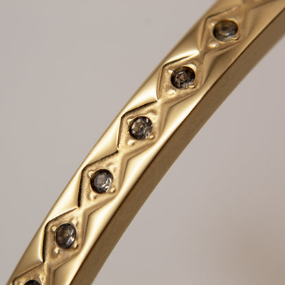 Gold bracelet with diamond-like stones on a gray background