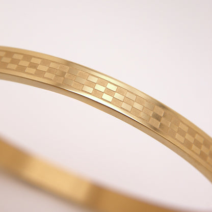 Gold bracelet with a checkered pattern on a light pink background