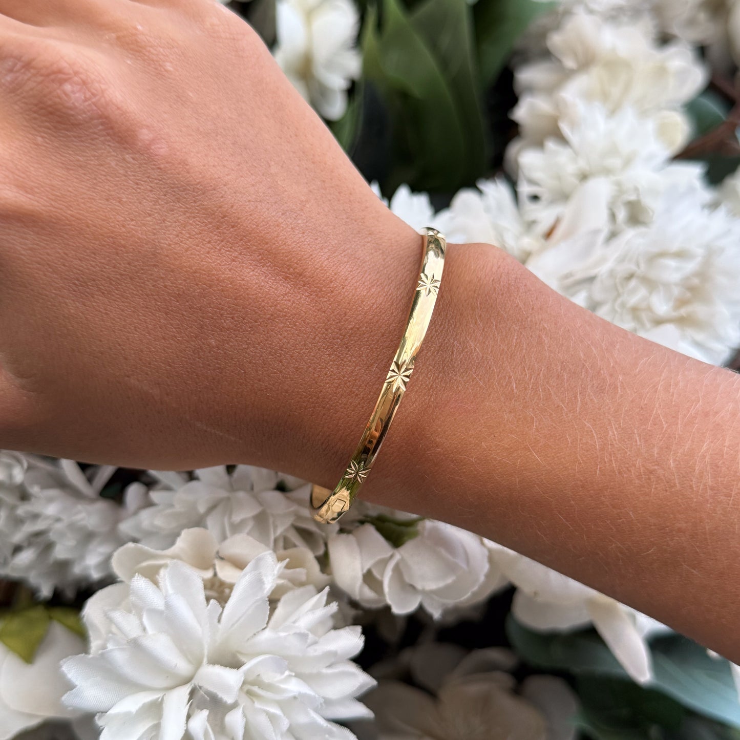 Gold bracelet on a wrist with a background of white flowers