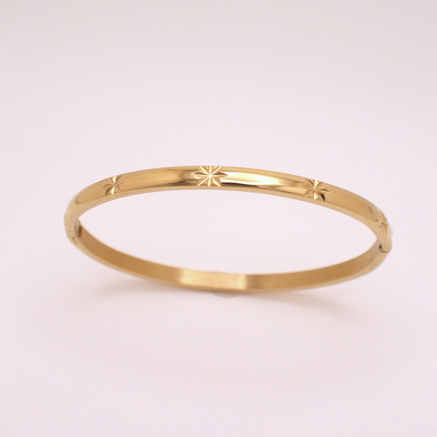 Gold bracelet with star design on a light pink background