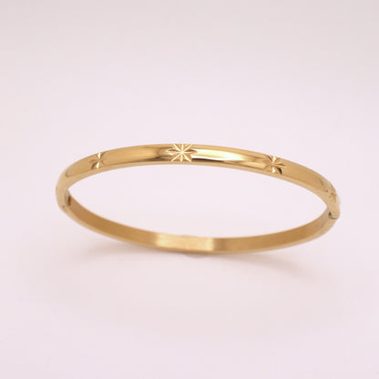Gold bracelet with star design on a light pink background