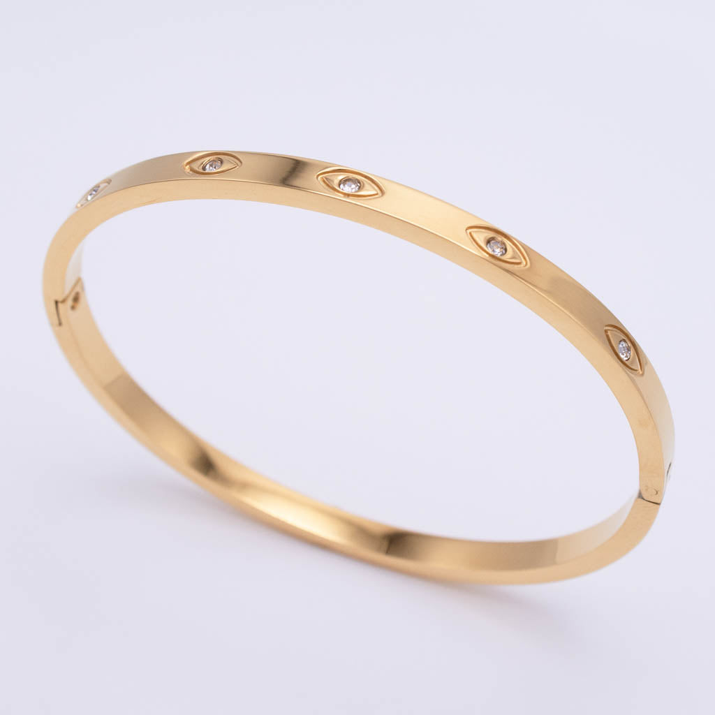 A gold bangle bracelet with small bezel-set clear stones arranged in a row, photographed on a clean white background.
