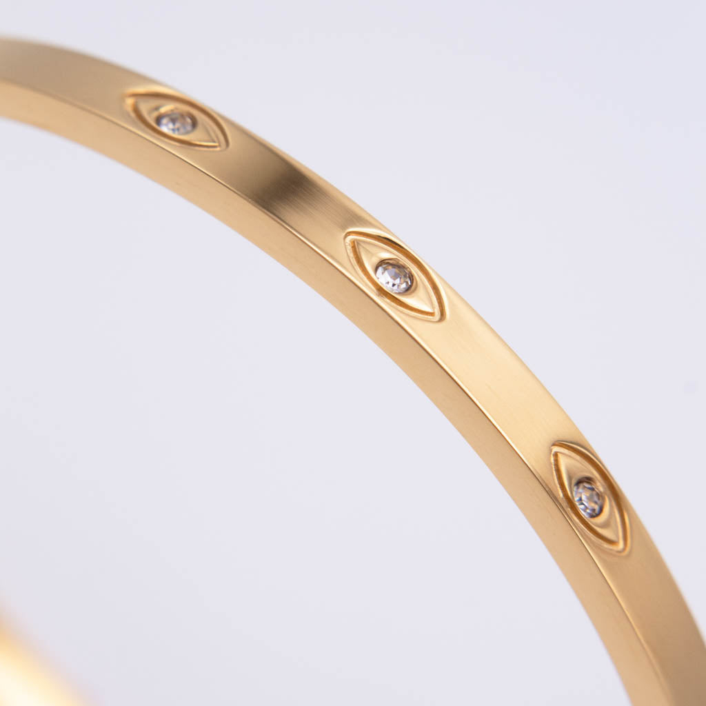 A close-up of a gold bangle bracelet featuring small oval-cut clear stones set into the band, photographed against a clean white background.
