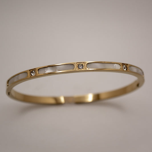 Gold bracelet with embedded stones on a light gray background