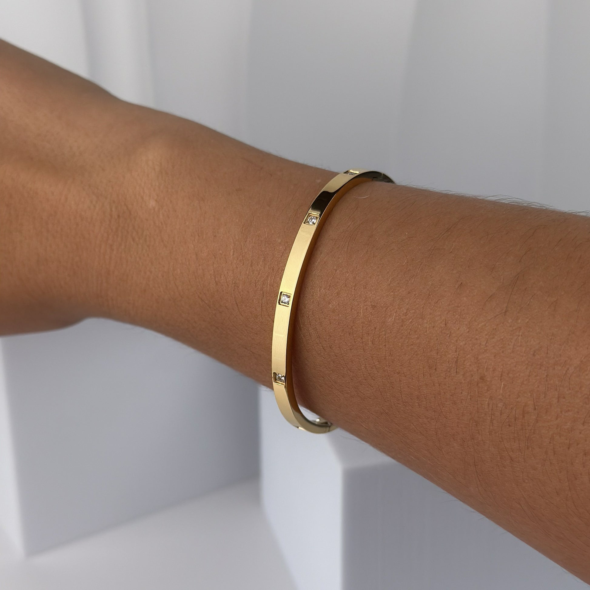 Gold bracelet with small diamonds on a wrist against a white background
