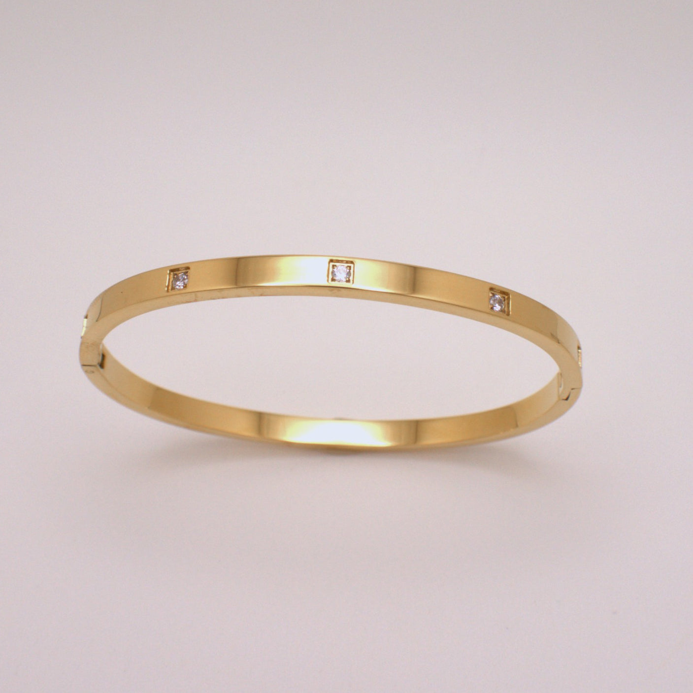 Gold bracelet with embedded diamonds on a light gray background