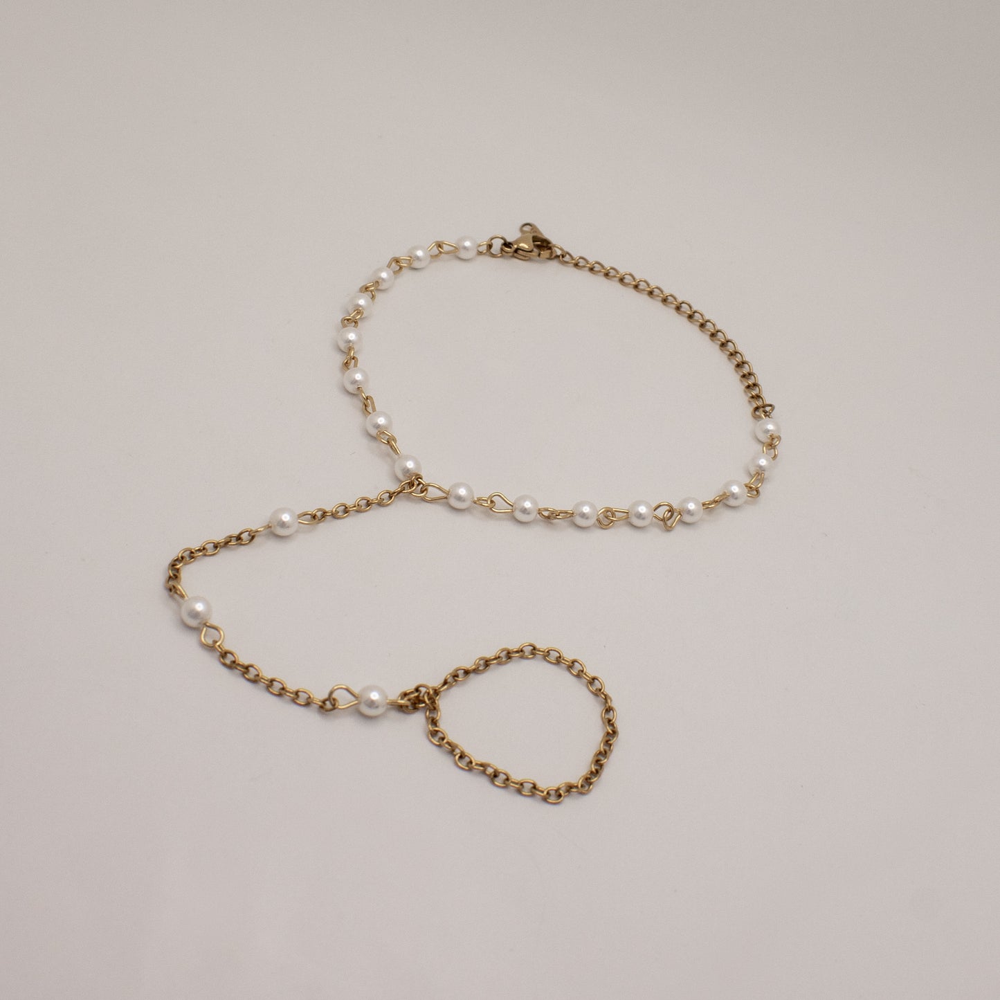 Gold chain bracelet with pearl beads on a light gray background