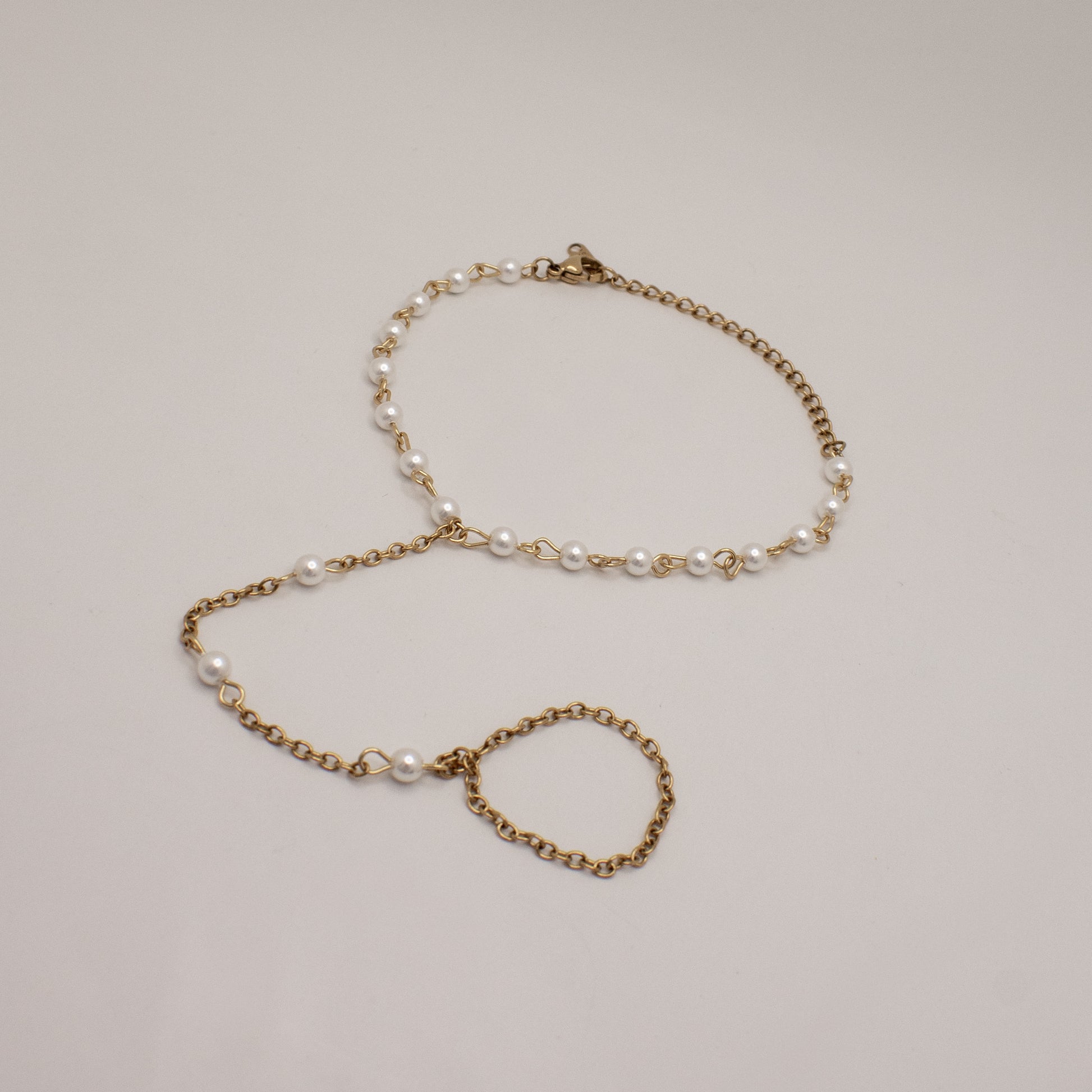 Gold chain bracelet with pearl beads on a light gray background