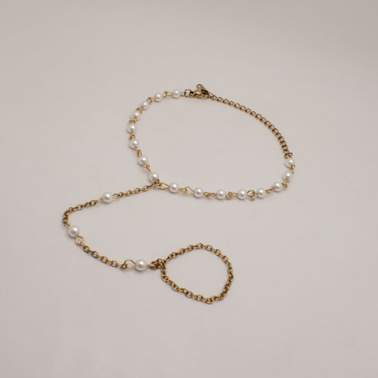 Gold chain bracelet with pearl beads on a light gray background