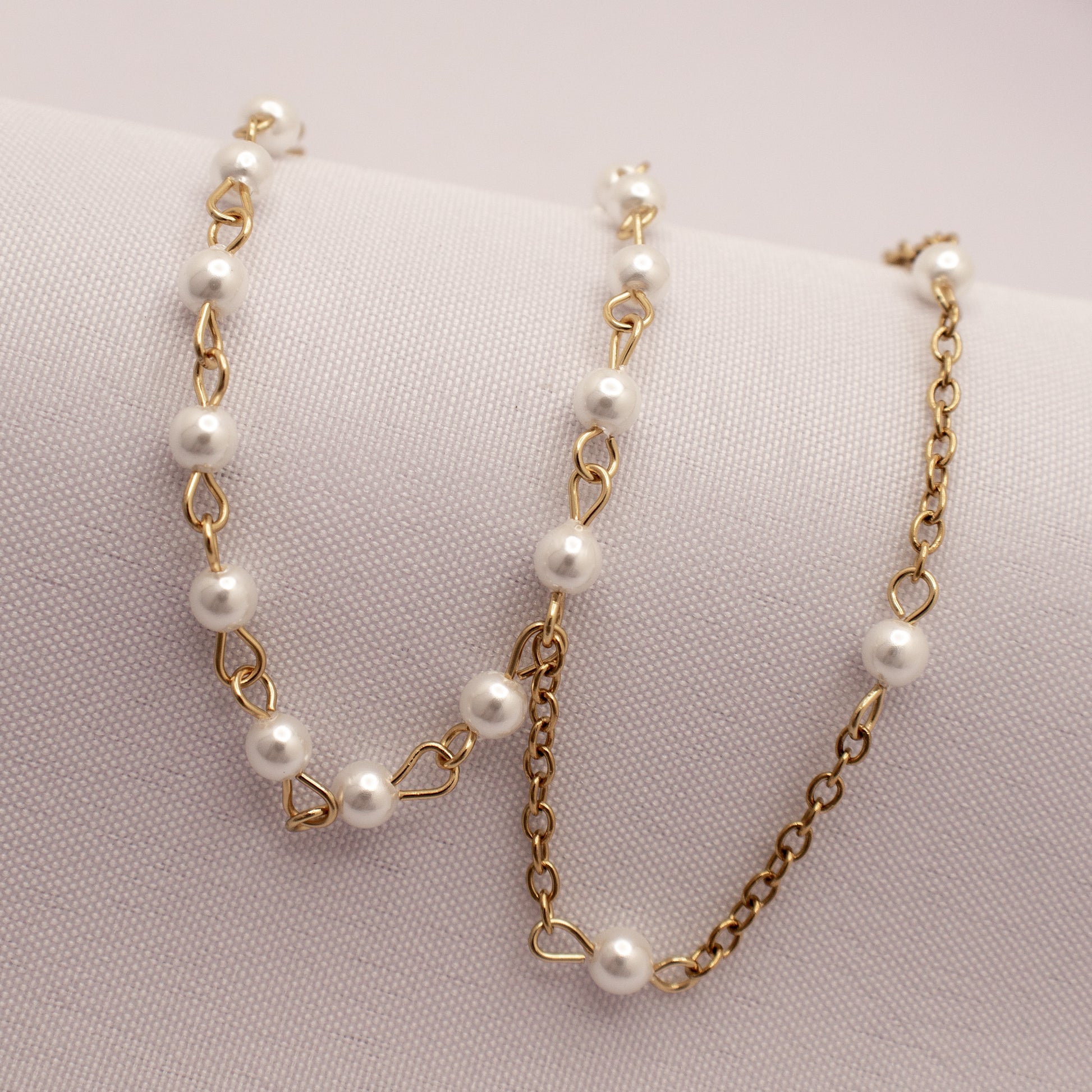 Gold chain bracelet with white pearls on a light pink background