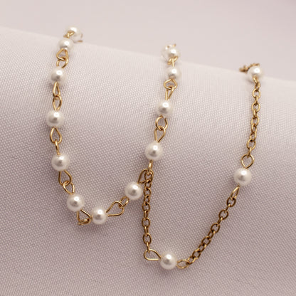 Gold chain bracelet with white pearls on a light pink background