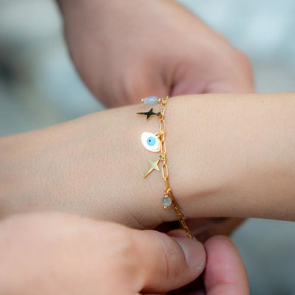 A gold chain bracelet with evil eye charms and star details worn on a person's wrist, shown in a close-up lifestyle shot.