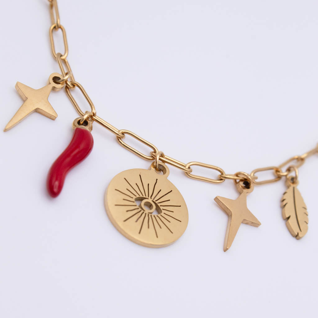 Gold-tone chain necklace with multiple charms, including a red curved charm, a round sunburst disc, and three star-like pendants, photographed on a clean white background.