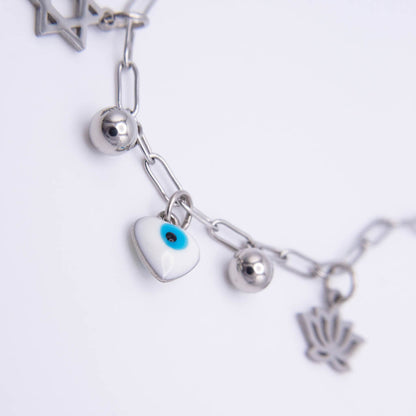 Silver-tone chain bracelet featuring a white evil eye heart charm with a blue and black eye, silver ball charms and a hamsa hand charm on a white background.