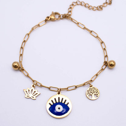 Gold chain anklet with three charms: a blue and white evil eye pendant, a gold lotus flower, and a gold tree of life, on a white background.