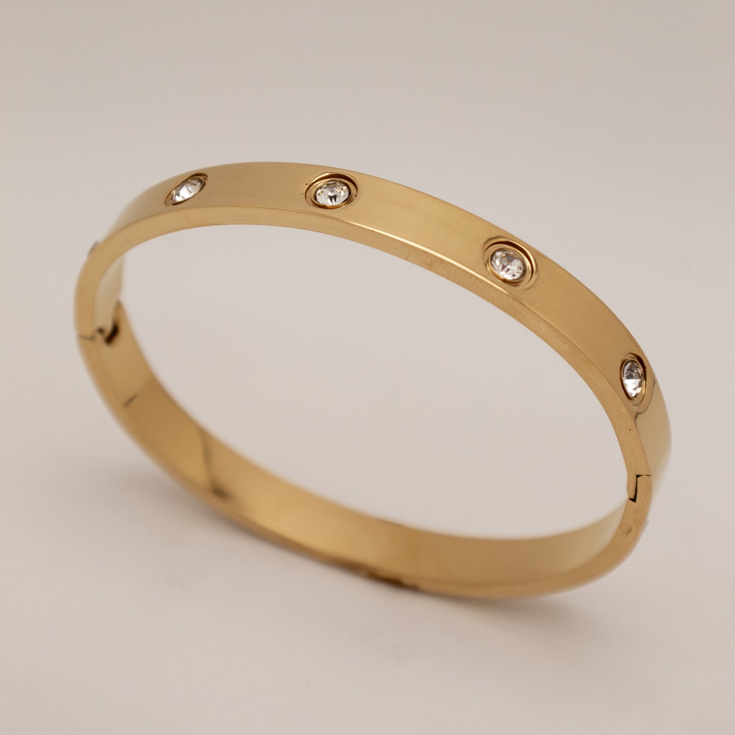 Gold bracelet with diamond-like stones on a light gray background