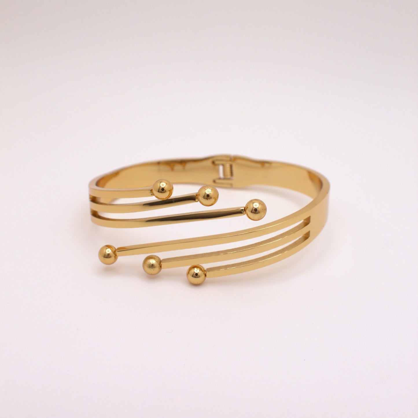 Gold bracelet with spherical accents on a light pink background