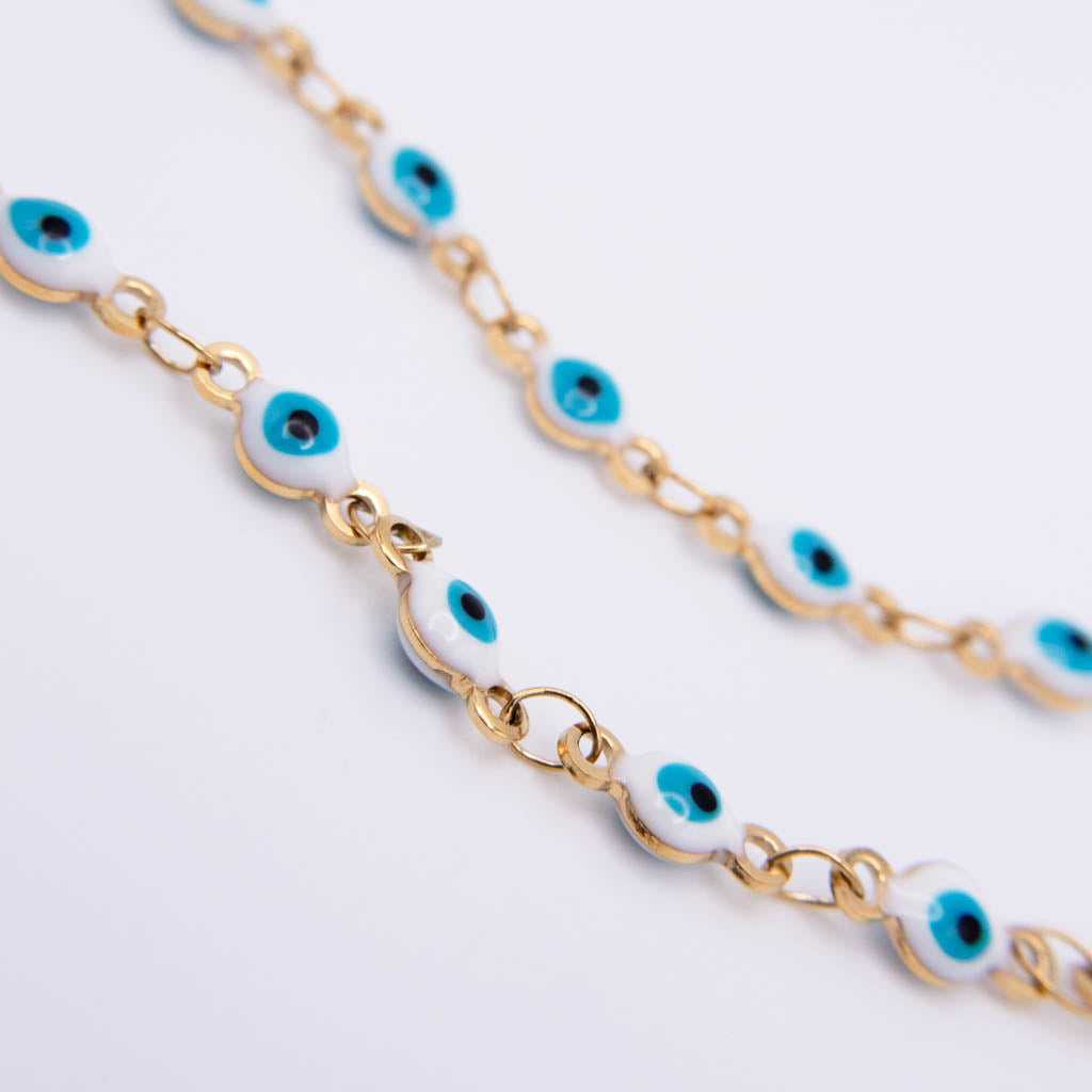 Gold chain bracelet with white enamel evil eye charms, photographed on a clean white background.