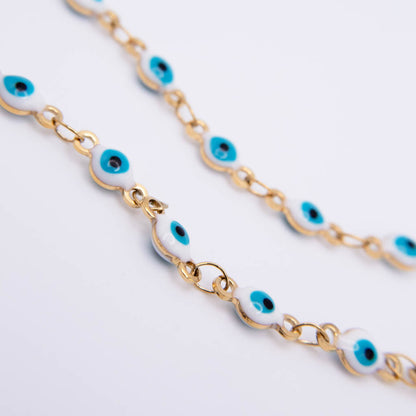 Gold chain bracelet with white enamel evil eye charms, photographed on a clean white background.