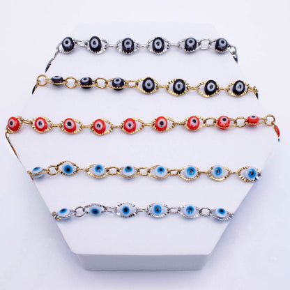 Five evil eye charm bracelets displayed on a white hexagonal stand. The bracelets feature black, red, and blue evil eye charms linked with silver and gold-tone metal chains.