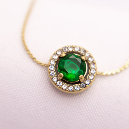 Necklace with a green gemstone and gold setting on a light pink background