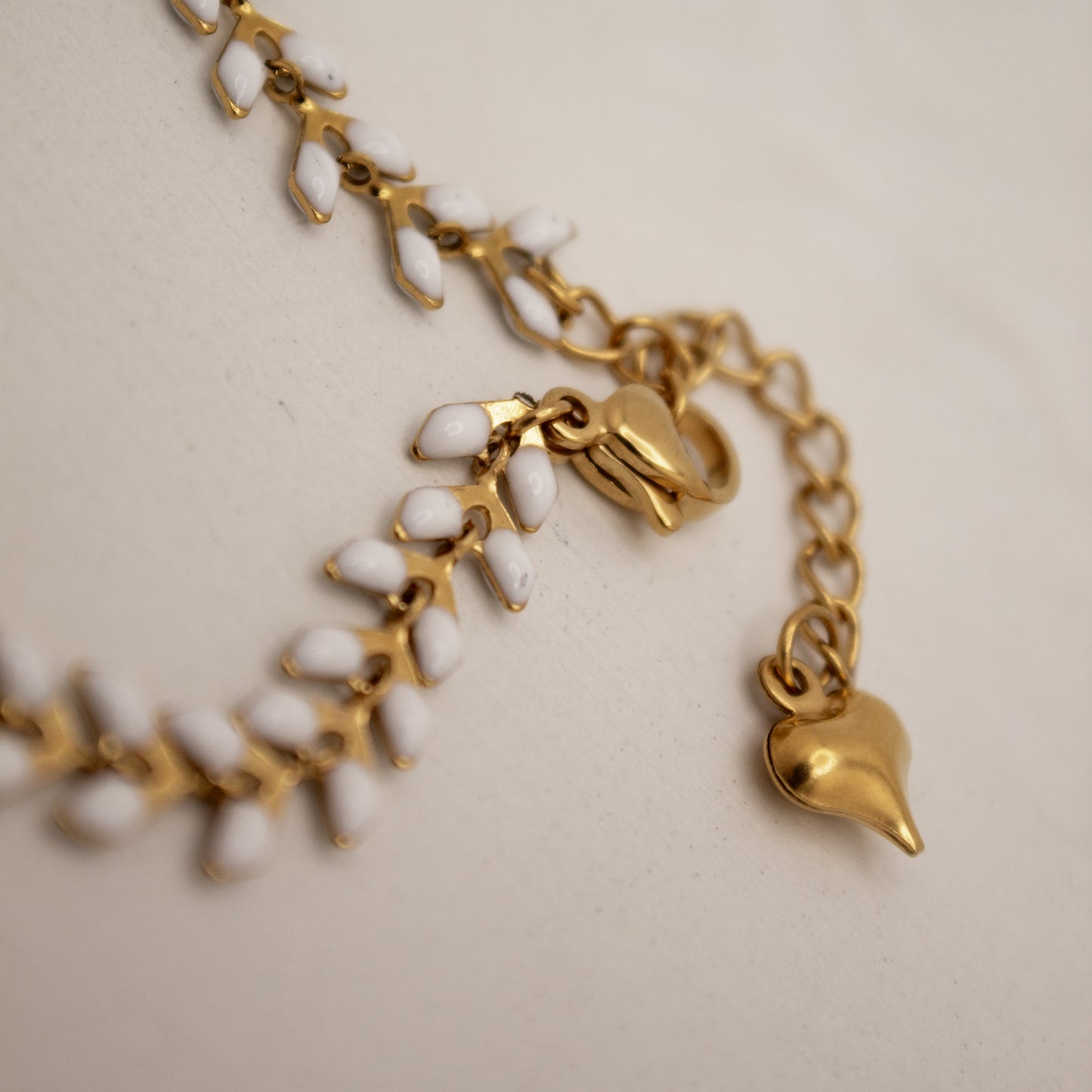 Gold bracelet with white beads and heart charm on a beige background