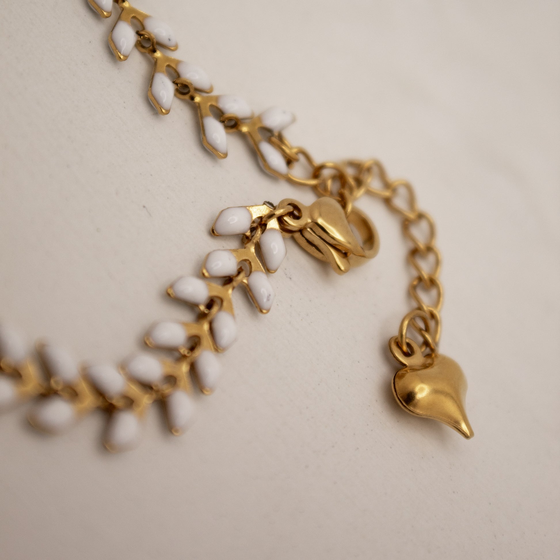 Gold bracelet with white beads and heart charm on a beige background