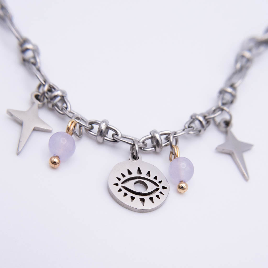 A silver-toned chain necklace featuring a central oval charm with an eye design, flanked by two lavender beads with gold spacer beads and two silver star charms, on a plain white background.