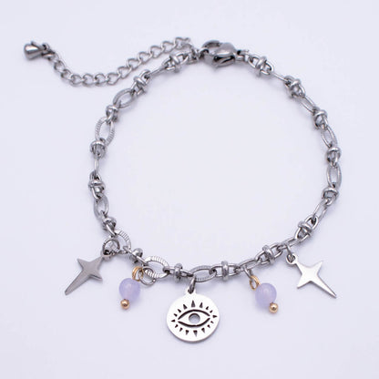 A silver-toned chain anklet featuring a central round charm with an eye design, flanked by two star charms, a small purple bead, and a tiny gold bead. The anklet is displayed on a clean white background.