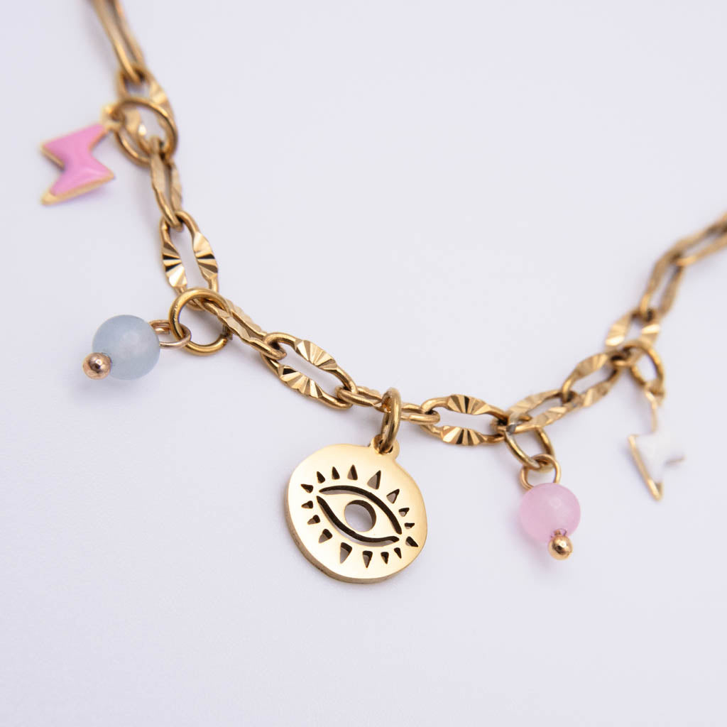 Gold-tone chain necklace with a central eye charm, pink enamel lightning bolt, pale blue bead, and pink bead charms on a white background.