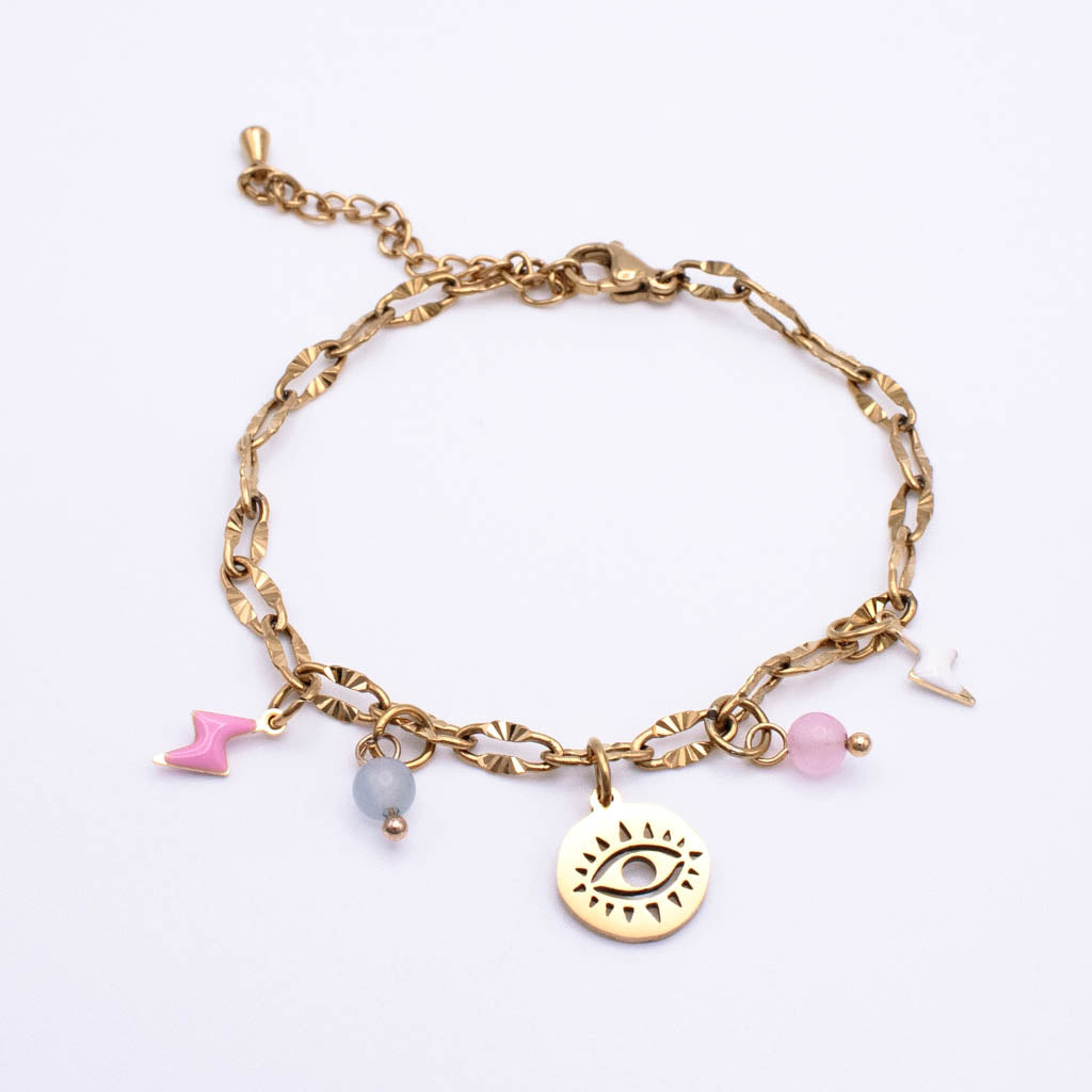 A gold chain anklet featuring a central round gold disc charm with an eye design, flanked by dangling charms including a pink chevron, a pale blue bead, a pink stone, and a small white charm, displayed on a clean white background.