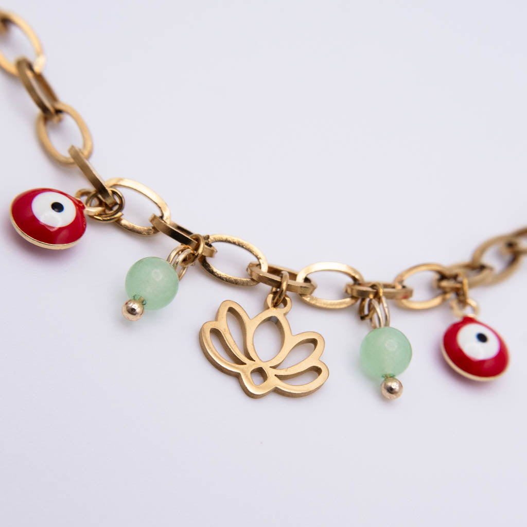 Gold-tone chain bracelet with evil eye charms, green beads, and a lotus flower charm on a white background.