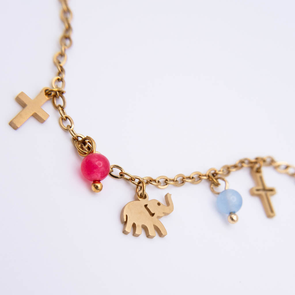 A gold-tone chain necklace featuring a small elephant charm, two cross charms, one pink bead, and one light blue bead on a clean white background.