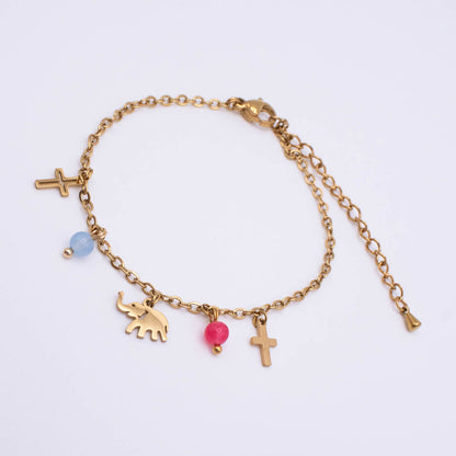 A gold chain bracelet with multiple charms, including two crosses, an elephant, a pink bead, and a light blue bead, displayed on a clean white background.