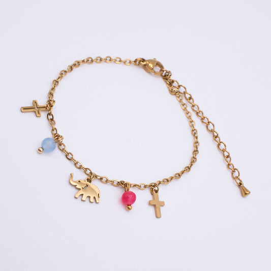 A gold chain bracelet with multiple charms, including two crosses, an elephant, a pink bead, and a light blue bead, displayed on a clean white background.