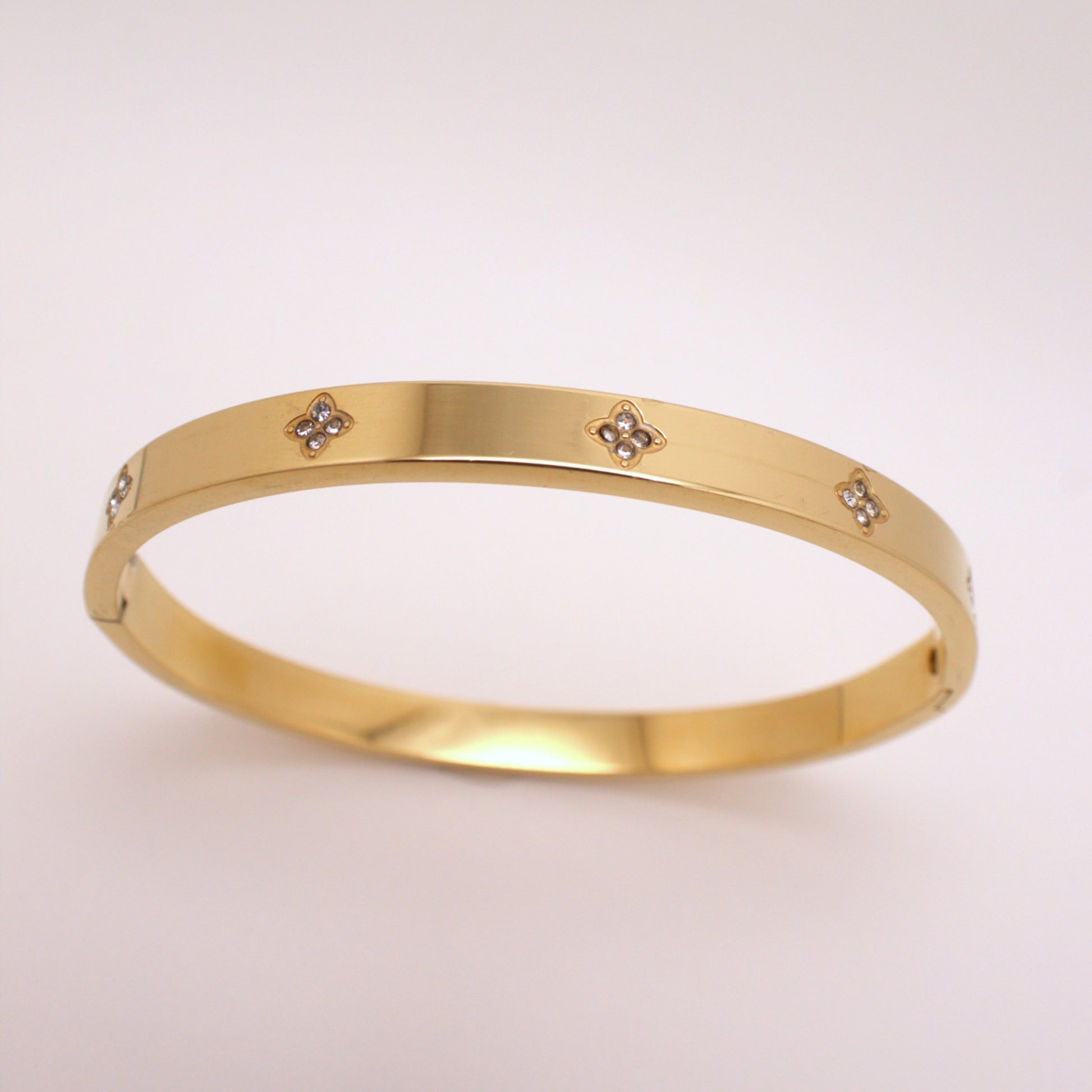 Gold bracelet with small diamond-like stones on a light pink background