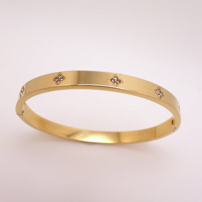 Gold bracelet with small diamond-like stones on a light pink background