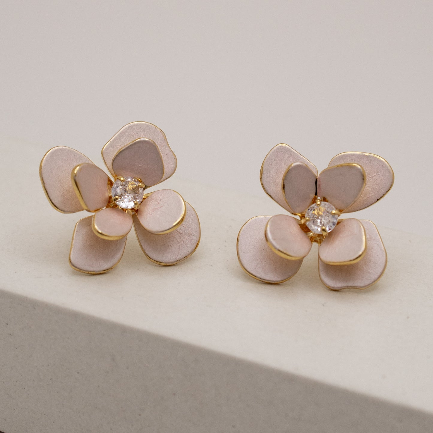 Flower-shaped earrings with pink petals and gold accents on a light gray background