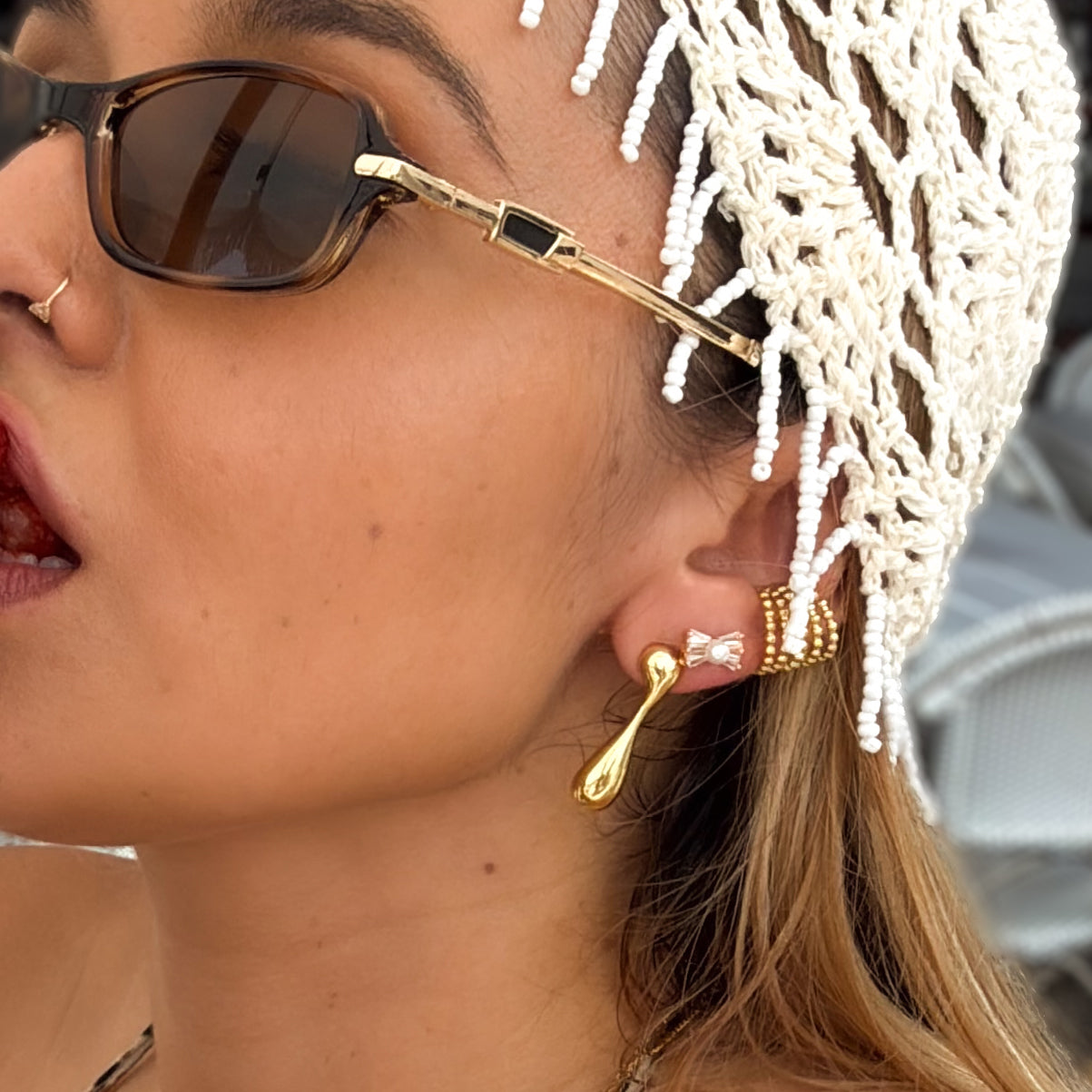 Close-up of a woman wearing gold earrings and sunglasses with a white headscarf.