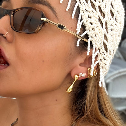 Close-up of a woman wearing gold earrings and sunglasses with a white headscarf.