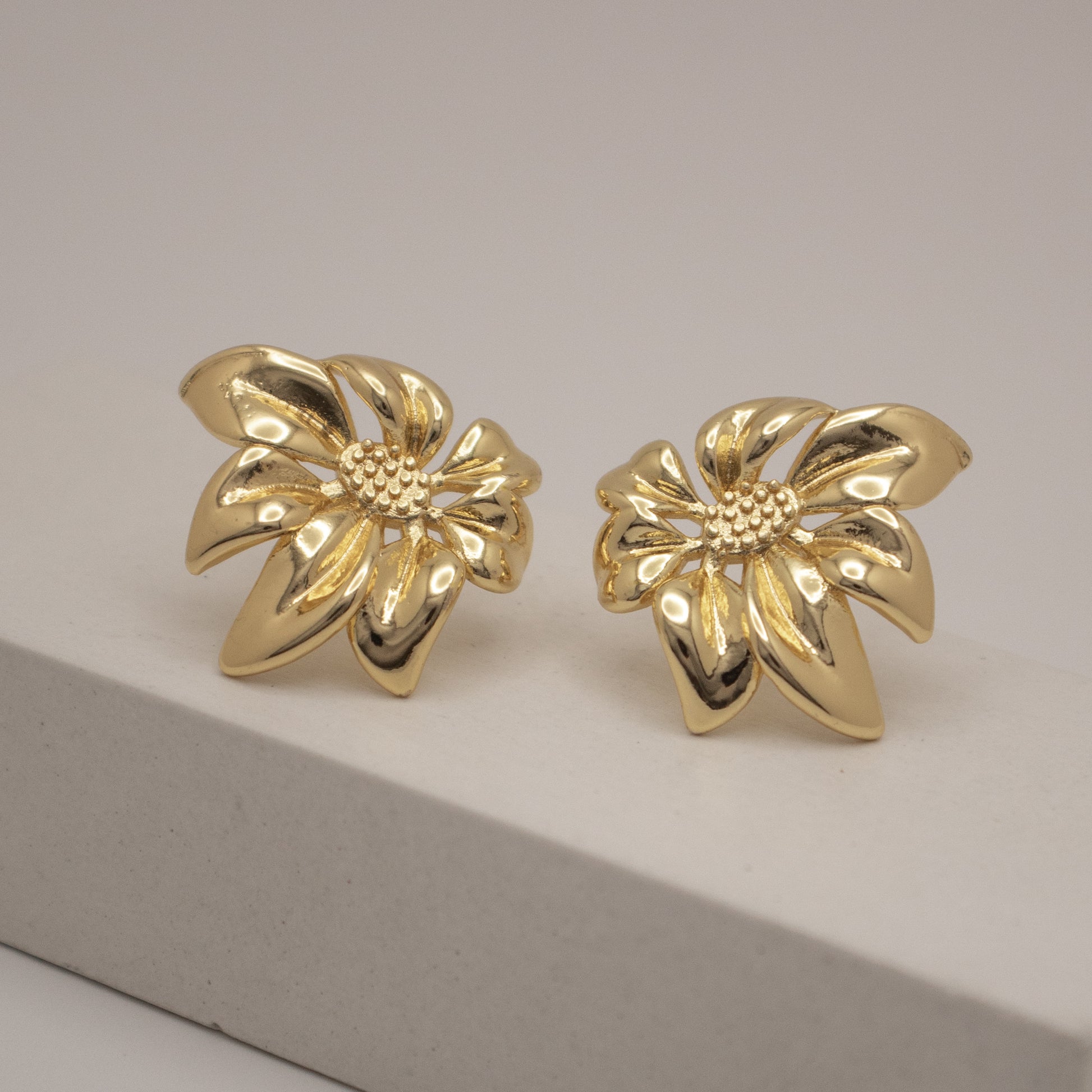 Pair of gold flower-shaped earrings on a gray surface