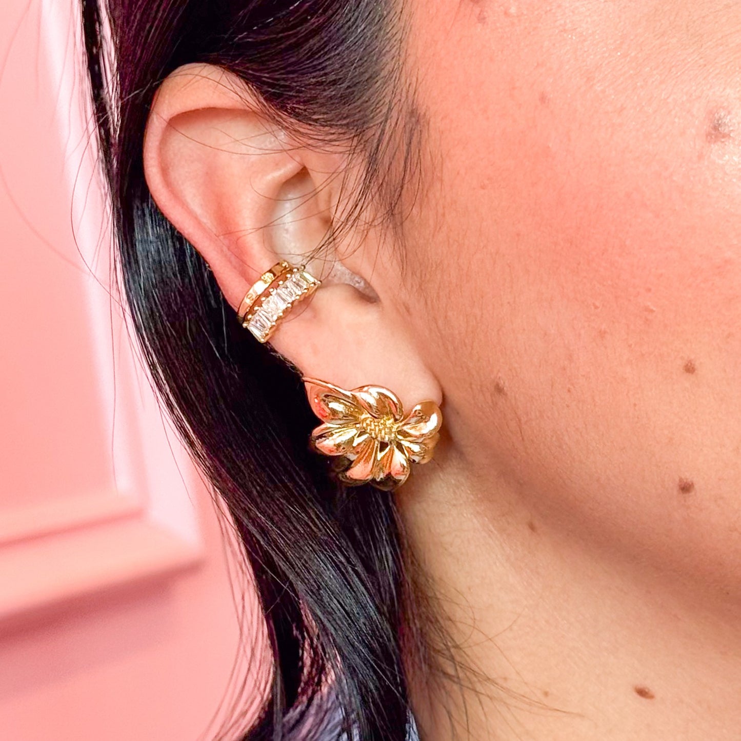 Close-up of a person wearing gold hoop earrings with a pink background
