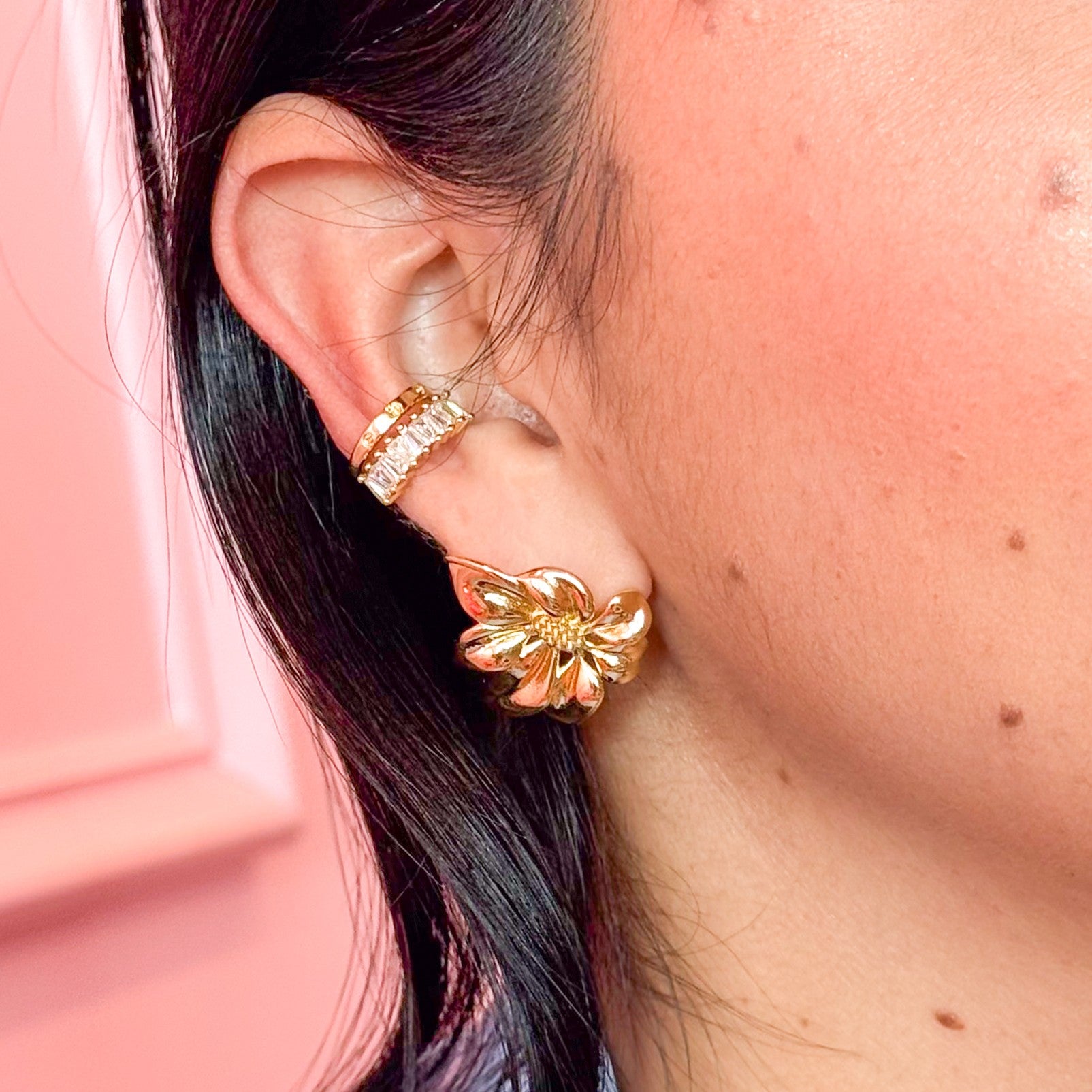 Close-up of a person wearing gold hoop earrings with a pink background