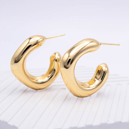 A pair of shiny gold abstract curved hoop earrings with post backs, displayed on a light gray textured surface.