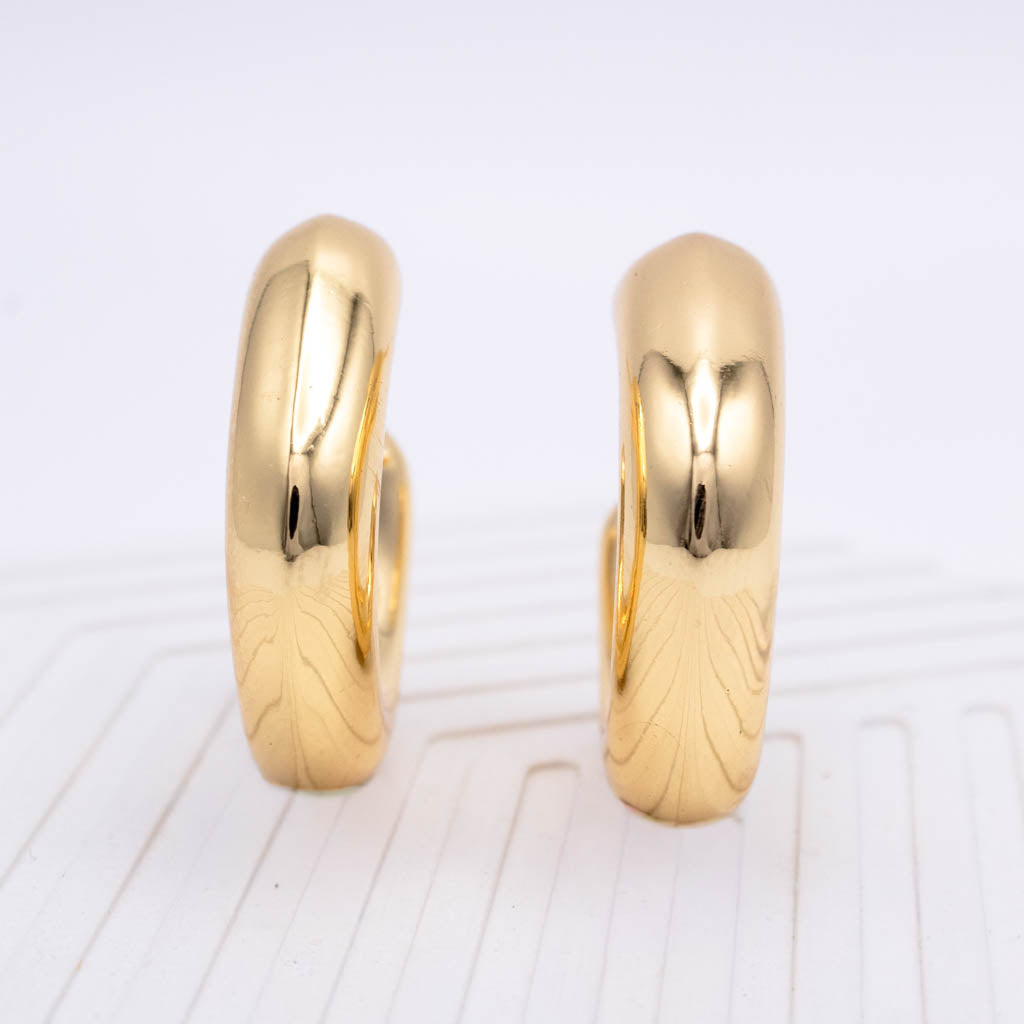 A pair of polished yellow gold hoop earrings standing upright on a white textured surface.