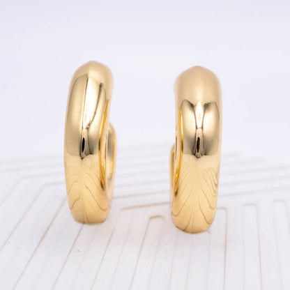 A pair of polished yellow gold hoop earrings standing upright on a white textured surface.