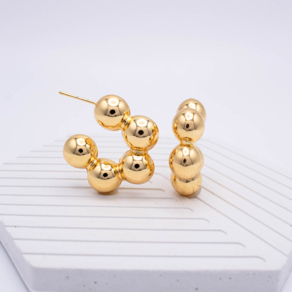 A pair of gold-toned beaded hoop earrings with a post back, displayed on a white ribbed surface against a light gray background.