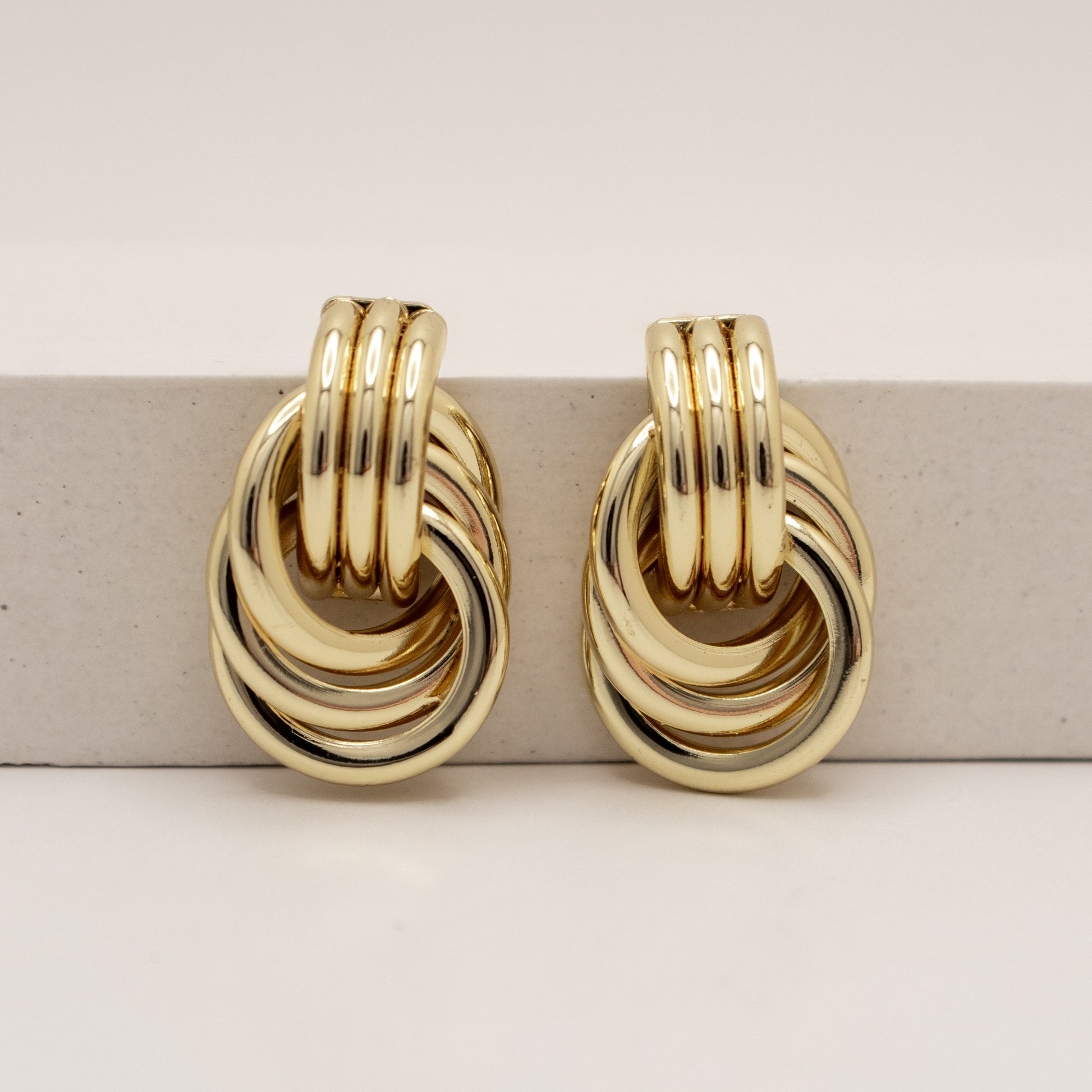 Gold hoop earrings on a light gray surface with a beige background
