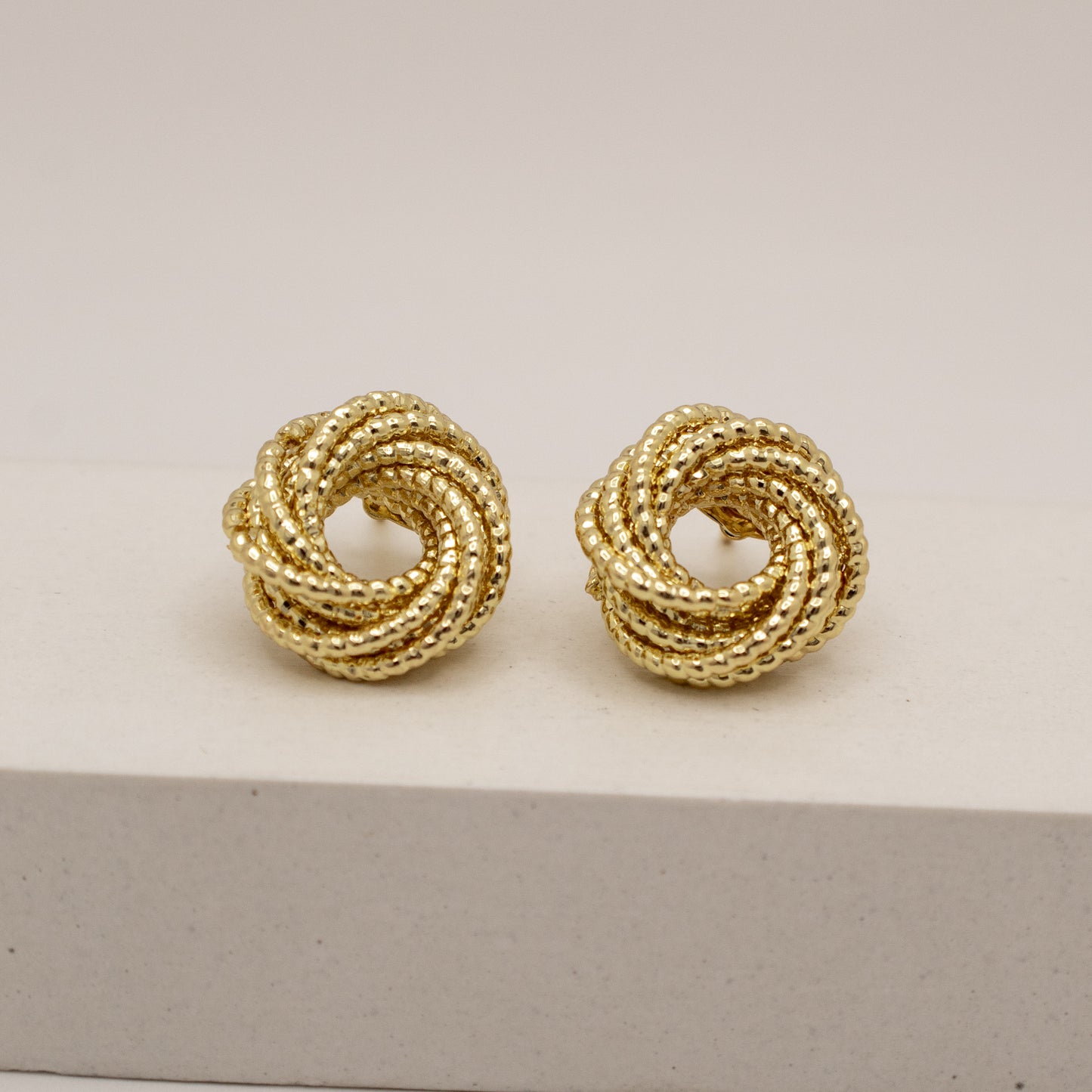Pair of gold knotted earrings on a light gray background